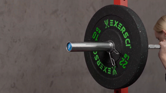 A close-up image of an Exersci 10 kg plate on an Olympic bar with a woman placing the bar on her upper back in a squat rack, to illustrate the Exersci blog post entitled 'What is a Good Budget for a Home Gym?'