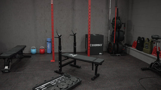 Image of a Bench, Squat rack and free weights in an Exersci branded home gym to illustrate the Exersci blog post entitled 'Free weights vs machines —  pros, cons, and which one reigns supreme?'